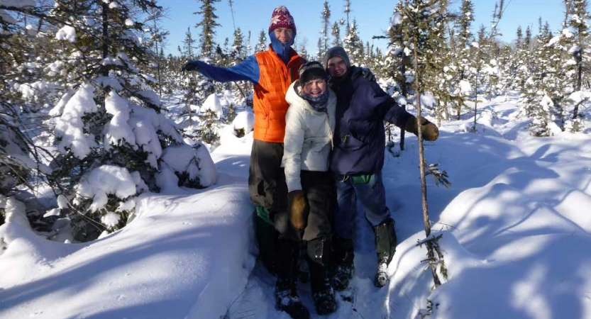 three people stand in deep snow surrounded by trees and smile at the camera 